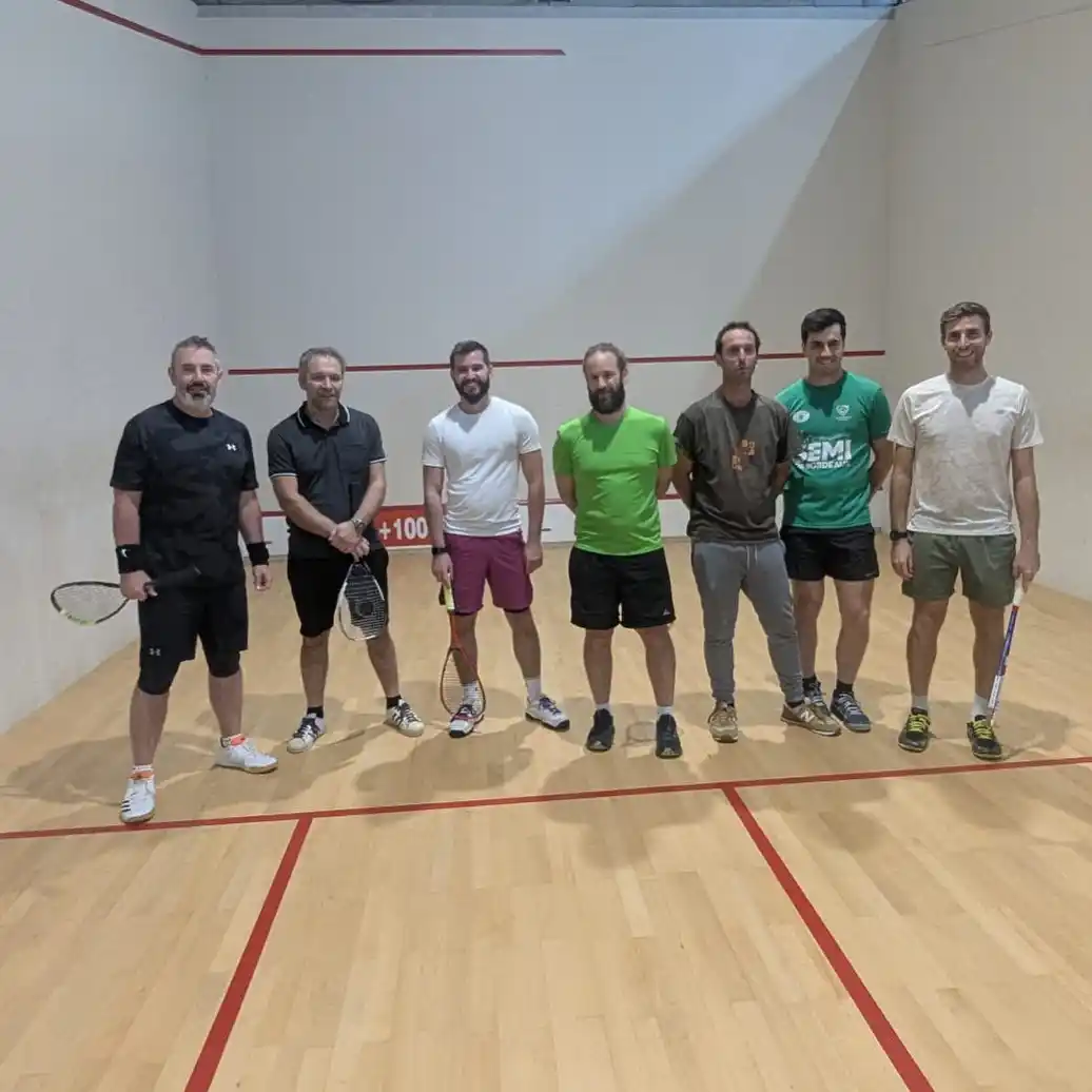 Groupe de joueurs posant dans un court de squash après une session ou un match.